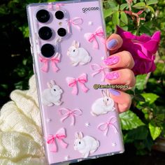 a person holding up a pink phone case with white rabbits and bows on the back