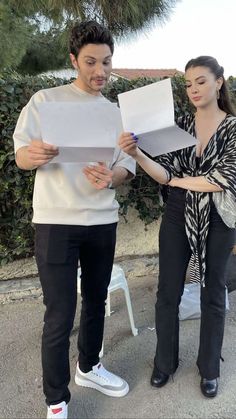 a man and woman standing next to each other while holding papers in front of them