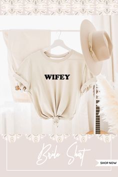 a white t - shirt with the words wife on it and a hat hanging from a rack