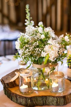 mason jars filled with white flowers sit on a wood slice at the center of a table