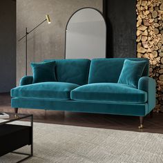 a blue couch sitting on top of a wooden floor next to a table and mirror