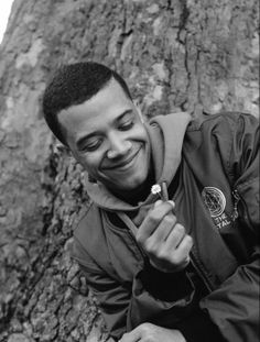 a man sitting next to a tree holding a piece of food in his hand and smiling at the camera