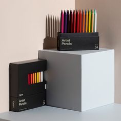 several different colored pencils are stacked on top of each other in front of a white box