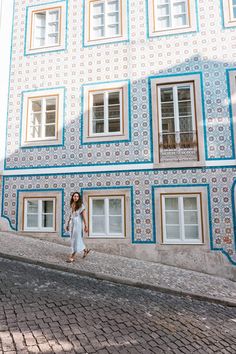 a woman is walking down the street in front of a building with blue and white tiles