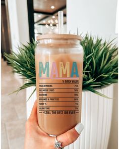 a person holding up a drink in front of a plant with the words mama on it