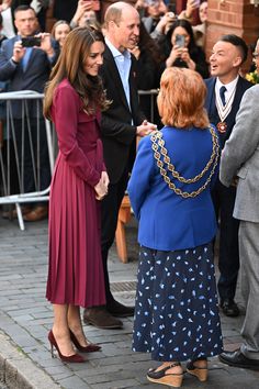 two women shaking hands in front of a group of people on the street with cameras around them