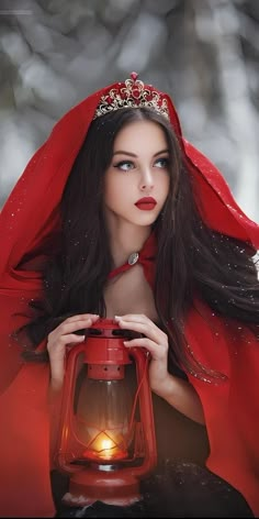 a woman wearing a red cape holding a lantern in her hands and looking at the camera