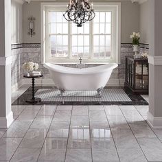 a white bath tub sitting under a window next to a chandelier in a bathroom