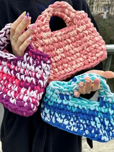 a woman holding three woven purses in her hands, one is pink and the other is blue