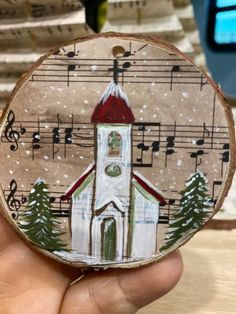 a hand holding a piece of wood with a painting of a church and music notes on it