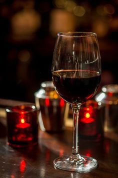 a glass of red wine sitting on top of a table next to two glasses filled with liquid