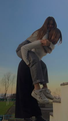 two girls are hugging on the edge of a bench in front of a blue sky