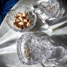 two glass dishes with nuts in them on a silver tableclothed surface next to a book