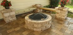 a fire pit sitting in the middle of a patio next to two planters and a bench