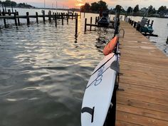 a white surfboard sitting on top of a wooden dock next to the water at sunset