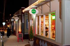 a city street at night with cars parked on the sidewalk and storefronts lit up