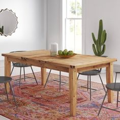 a dining table with two chairs and a bowl of fruit on it in front of a potted cactus