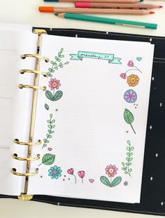 an open notebook with flowers and leaves on the cover, next to colored pencils