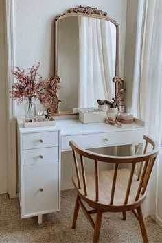 a white desk with a mirror, chair and vase on it in front of a window