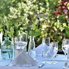 the table is set with glasses, silverware and flowers in vases on it