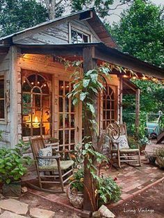 a porch with rocking chairs and lights on the outside, surrounded by plants and trees