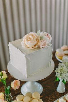 a white cake sitting on top of a wooden table next to flowers and desserts