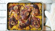 a pan filled with meat and vegetables on top of a white wooden table next to a napkin