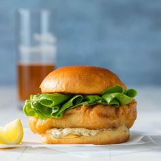 a chicken sandwich with lettuce and cheese next to a glass of beer on a table