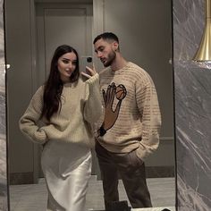 a man and woman standing in front of a mirror taking a selfie with their cell phone