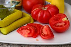 tomatoes, cucumbers, and pickles on a plate with mustard in the background