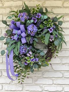 a wreath with purple flowers and green leaves hanging on a brick wall in front of a door