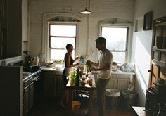 a man and woman standing in a kitchen next to each other with pots on the stove