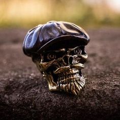 a close up of a skull wearing a hat on top of a dirt ground with trees in the background