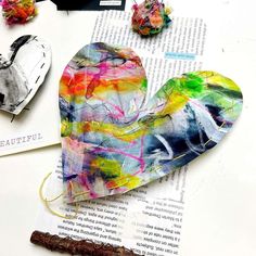 an altered paper heart sitting on top of a book next to some crafting supplies