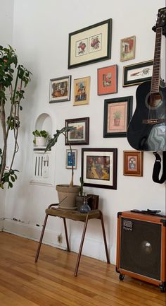 there is a guitar on the floor in front of a wall with pictures and plants