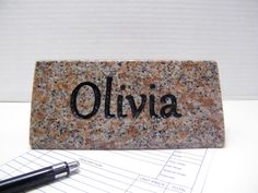 a stone with the word olivia on it next to a pen and paper