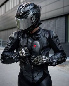 a person wearing a motorcycle suit and helmet with their hands on their hips, standing in front of a building