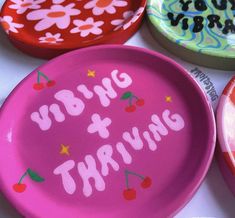 colorful plates with writing on them are sitting on a tablecloth covered surface, one is pink and the other is red