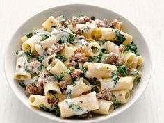 a white bowl filled with pasta, meat and spinach covered in cream sauce on top of a wooden table