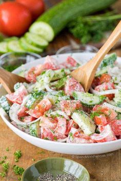 a salad with cucumbers, tomatoes and parsley in a white bowl on a wooden table