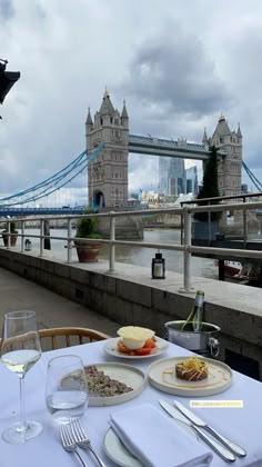 the table is set with plates and silverware for two people to eat in front of the tower bridge