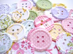 many different colored buttons on a white surface with pink, yellow and green flowers in the center