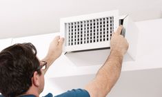 a man adjusting the air vent on a wall mounted heater in a room with white walls