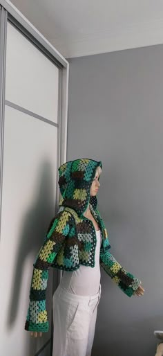 a woman standing in front of a door wearing a green jacket and white pants with crocheted patterns on it