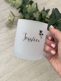 a person holding a white coffee mug with the word jesus written on it in black ink