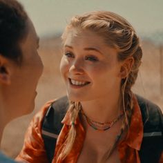 a woman with braids talking to another man in the desert, wearing an orange shirt