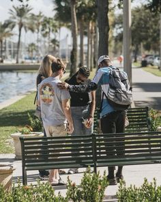 three people are standing near a park bench and looking at something on the other side