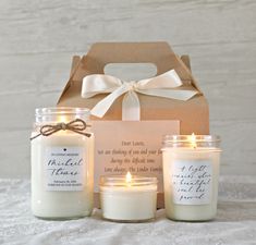 three candles are sitting in front of a box with a ribbon on it and the candle is lit