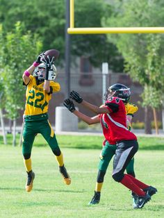 two young boys are playing football on the field with one holding his arm up in the air