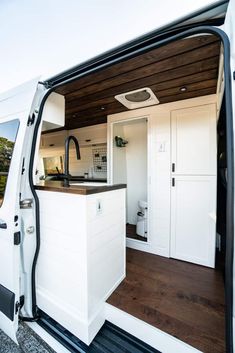 the interior of a white van with wood flooring and doors open to reveal a kitchen